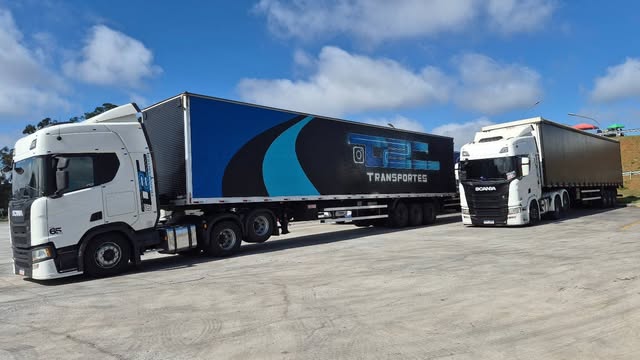 Caminhões reais da D2C, com carreta azul identificada com a marca da transportadora